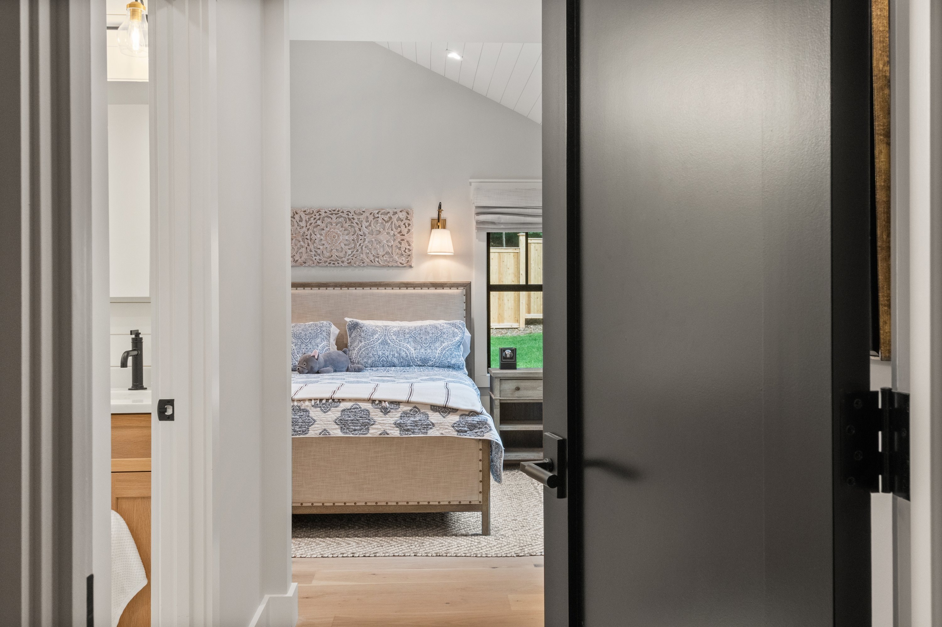 Bedroom viewed through doorway with shiplap ceiling, wall sconce, and black hardware