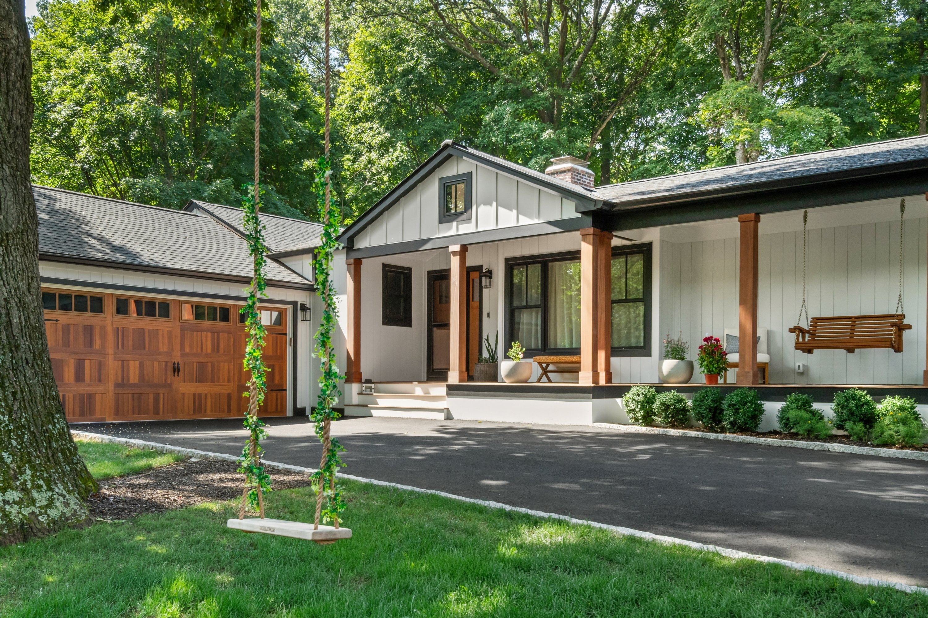 Modern farmhouse with cedar garage doors, covered porch, and tree swing