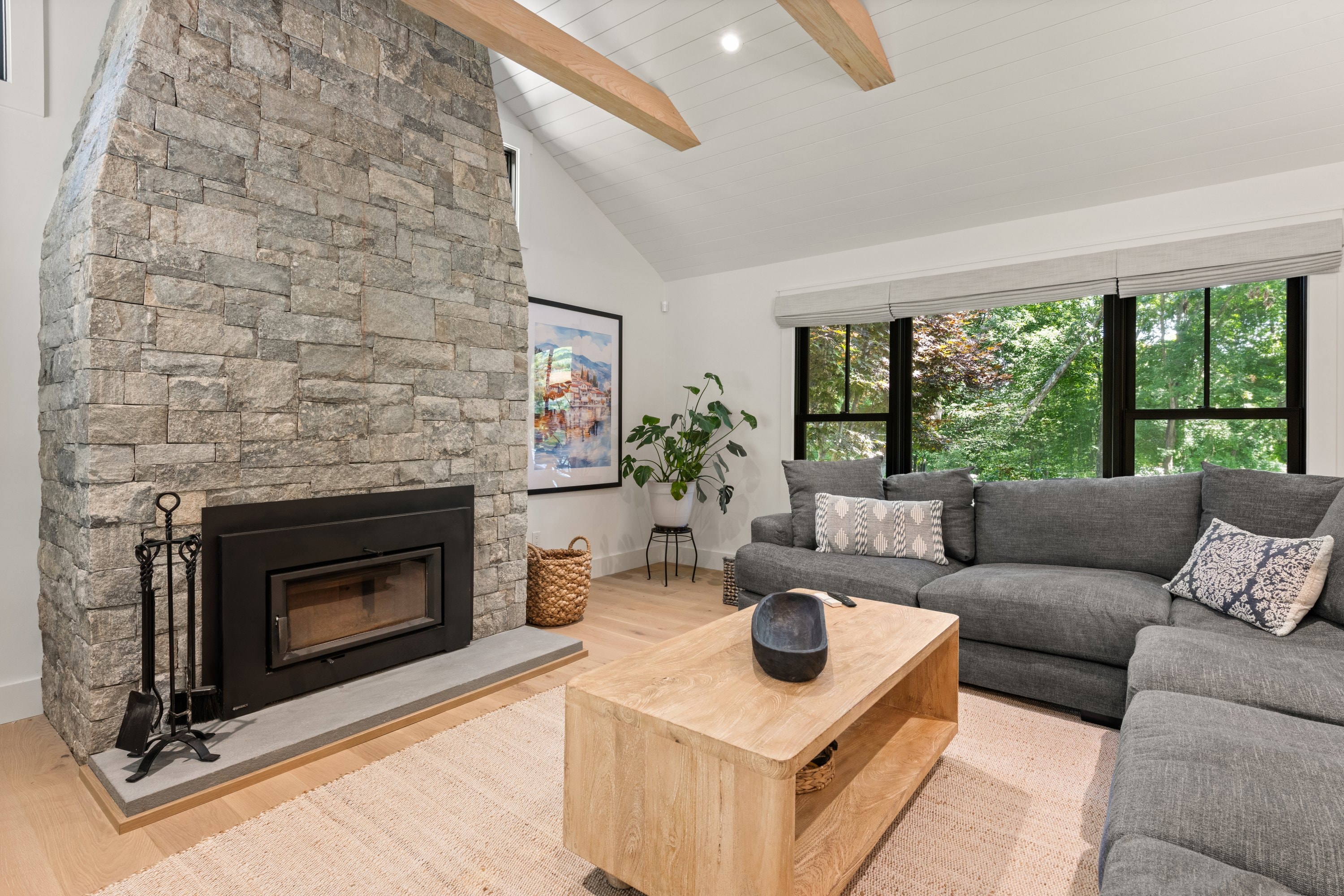 Living room with floor-to-ceiling stone fireplace, exposed beam, and hardwood floors