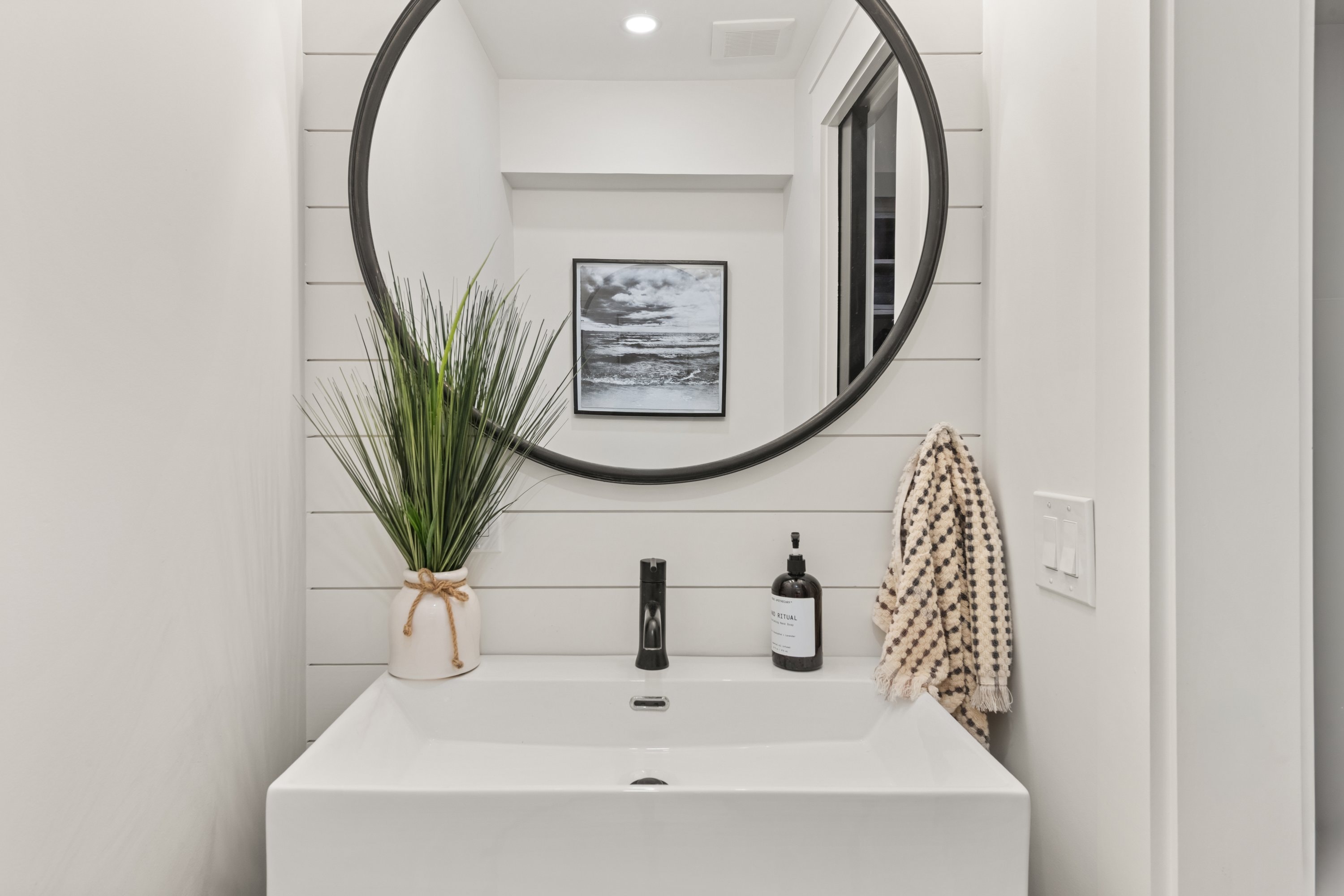 Powder room with shiplap walls, round black-framed mirror, and vessel sink