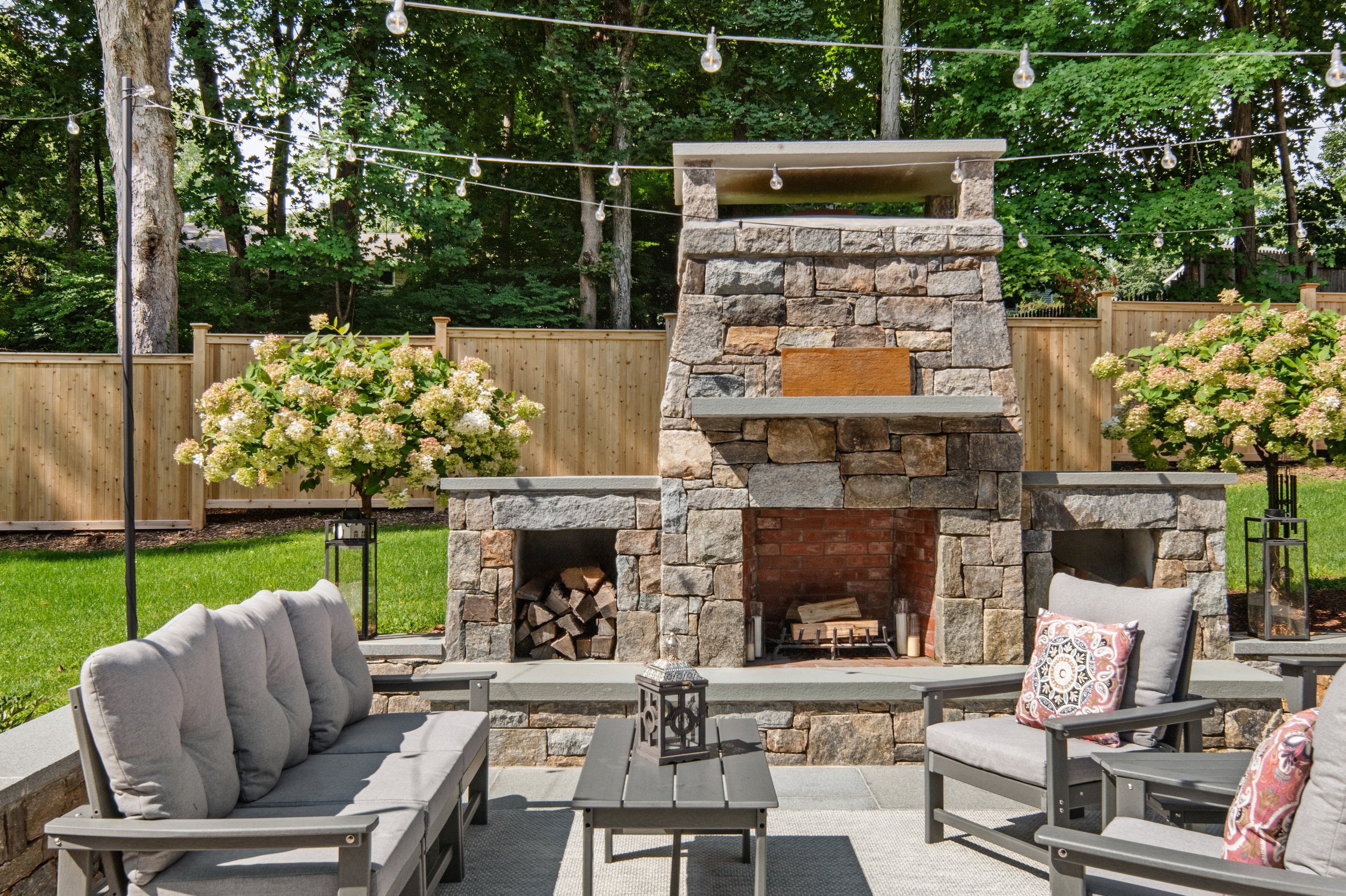 Custom stone outdoor fireplace with string lights and landscaped backyard